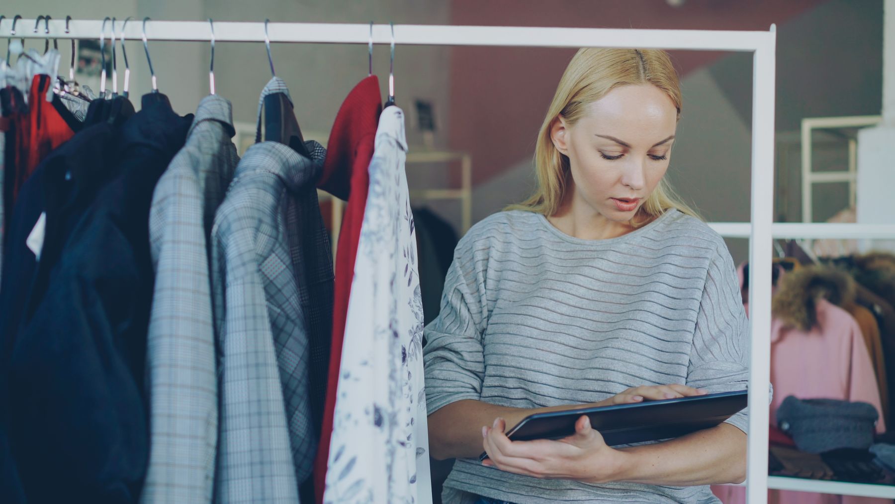 Retail employee using a tablet to review inventory inside a clothing store